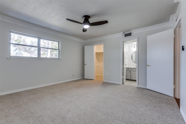 unfurnished bedroom featuring visible vents, light colored carpet, ornamental molding, a walk in closet, and a textured ceiling