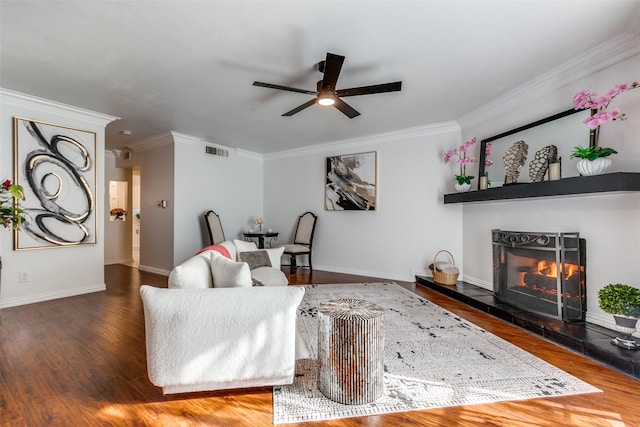 living area with a warm lit fireplace, dark wood-style floors, visible vents, and crown molding