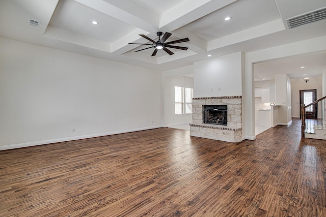 unfurnished living room featuring coffered ceiling, a stone fireplace, ceiling fan, dark hardwood / wood-style flooring, and beam ceiling