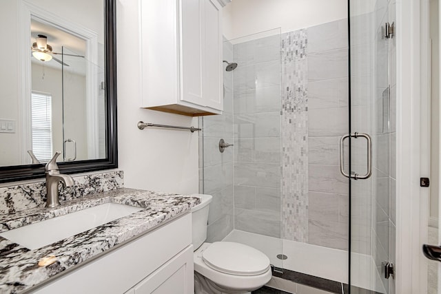 bathroom featuring toilet, ceiling fan, a shower with door, and vanity