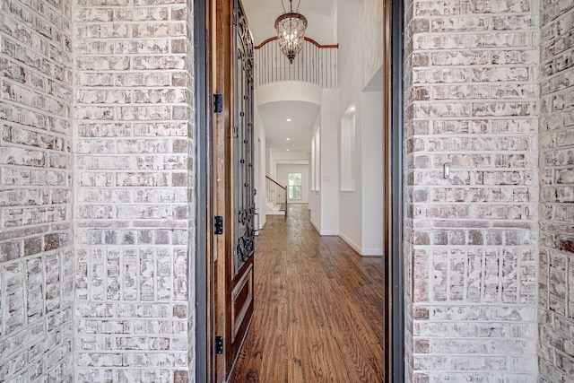 hall with a high ceiling, brick wall, dark hardwood / wood-style floors, and a notable chandelier