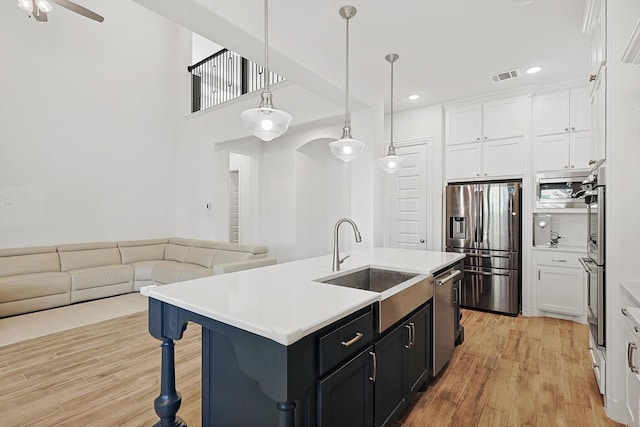 kitchen with sink, a center island with sink, appliances with stainless steel finishes, pendant lighting, and white cabinets