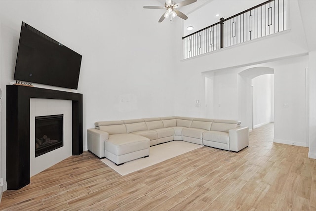 living room with a towering ceiling, ceiling fan, and light wood-type flooring