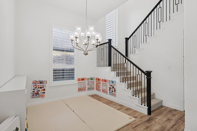 stairs featuring hardwood / wood-style flooring, radiator heating unit, a wealth of natural light, and a notable chandelier