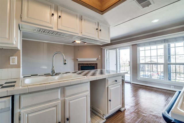 kitchen featuring sink, crown molding, tile counters, a fireplace, and white cabinets