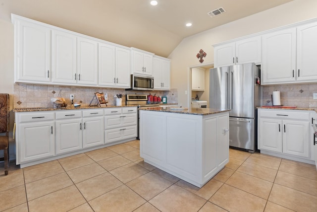 kitchen featuring light tile patterned floors, stainless steel appliances, white cabinetry, a center island, and dark stone counters