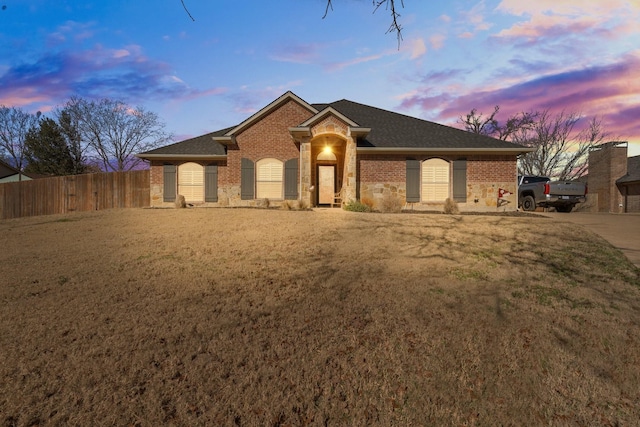 ranch-style house featuring brick siding, a front yard, fence, and a shingled roof