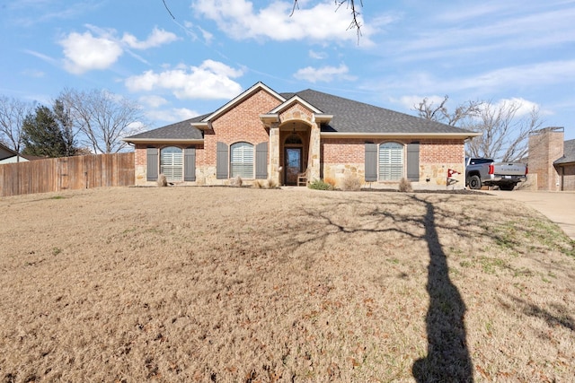 ranch-style home with brick siding, fence, a front lawn, and roof with shingles