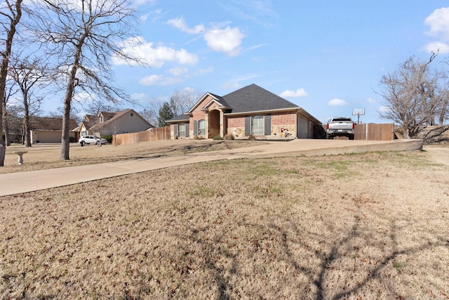 view of front of property featuring a front yard, fence, concrete driveway, and brick siding