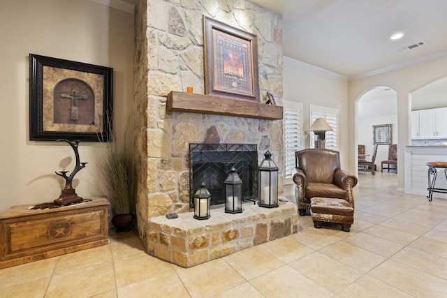 living room featuring a stone fireplace, ornamental molding, light tile patterned flooring, and visible vents