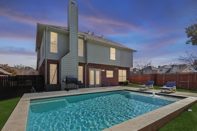 back house at dusk with a fenced in pool and a patio area