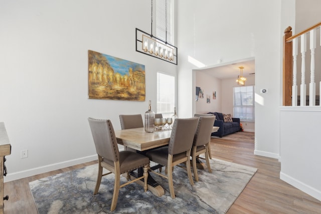 dining room featuring wood-type flooring, a towering ceiling, and an inviting chandelier