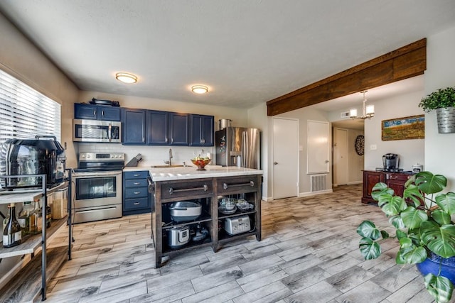 kitchen featuring blue cabinetry, sink, hanging light fixtures, stainless steel appliances, and a notable chandelier