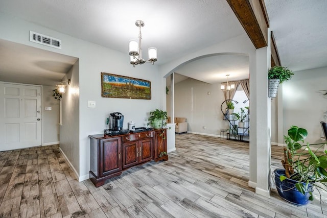 interior space with light hardwood / wood-style flooring, beamed ceiling, and a chandelier