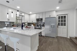 kitchen with white refrigerator with ice dispenser, backsplash, white cabinetry, and stainless steel range with electric cooktop