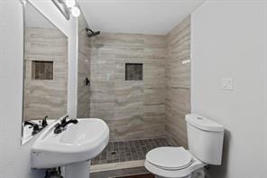 bathroom featuring toilet, sink, and a tile shower