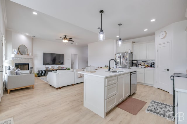 kitchen featuring white cabinetry, sink, stainless steel appliances, pendant lighting, and a kitchen island with sink