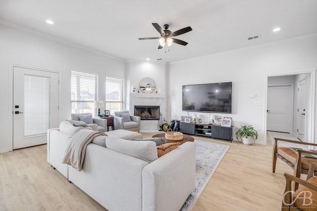 living room featuring a tile fireplace, crown molding, and light wood-type flooring