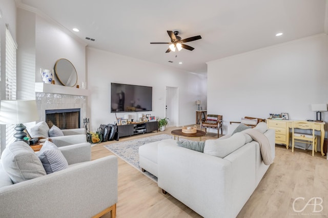 living room with ceiling fan, light hardwood / wood-style floors, crown molding, and a tile fireplace