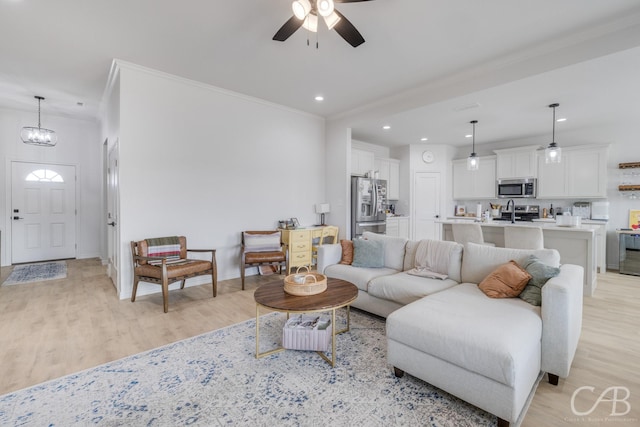 living room featuring sink, light hardwood / wood-style floors, ceiling fan with notable chandelier, and ornamental molding