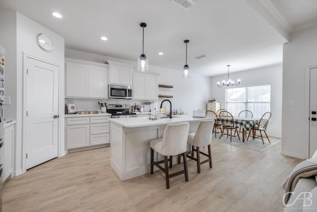 kitchen with white cabinets, pendant lighting, an island with sink, and appliances with stainless steel finishes