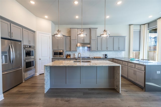 kitchen with gray cabinetry, appliances with stainless steel finishes, tasteful backsplash, decorative light fixtures, and light stone counters