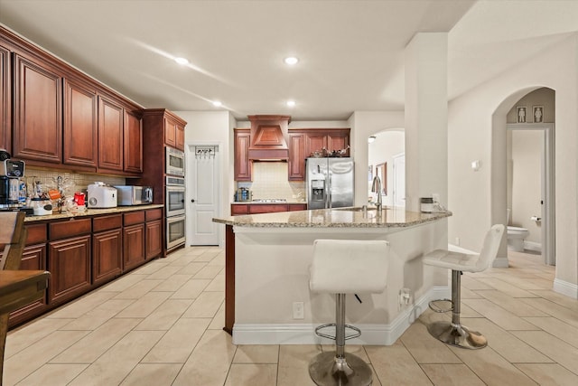 kitchen with stainless steel appliances, backsplash, a breakfast bar, light tile patterned floors, and custom range hood