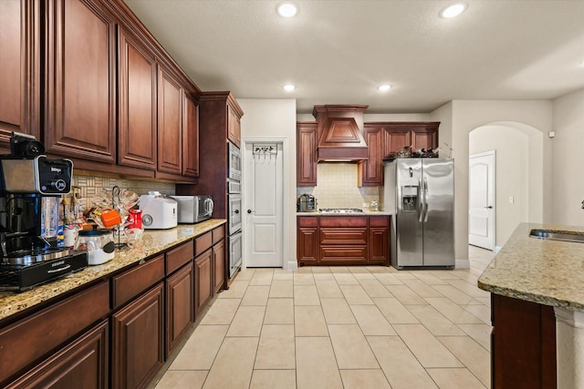 kitchen featuring sink, stainless steel appliances, tasteful backsplash, light stone counters, and custom exhaust hood