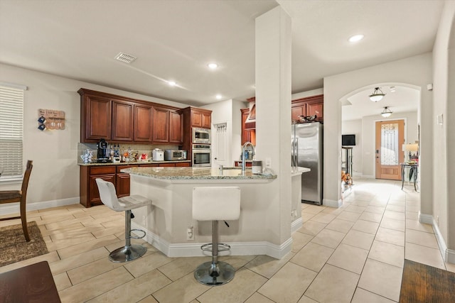 kitchen with a kitchen breakfast bar, sink, light tile patterned floors, light stone countertops, and appliances with stainless steel finishes