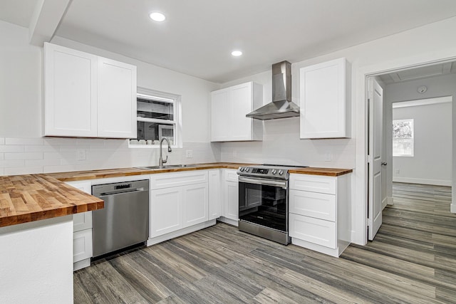 kitchen with butcher block counters, sink, wall chimney exhaust hood, appliances with stainless steel finishes, and white cabinetry