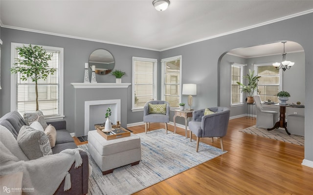 living room with wood-type flooring, ornamental molding, a wealth of natural light, and a chandelier