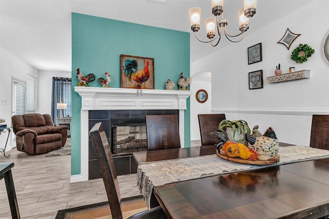 dining space with a tile fireplace, light hardwood / wood-style flooring, and an inviting chandelier