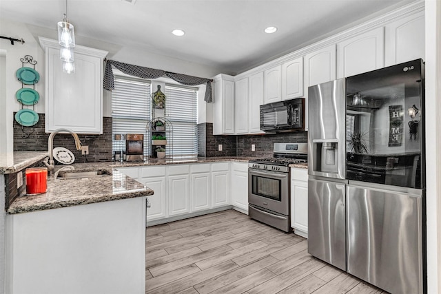 kitchen with dark stone counters, stainless steel appliances, sink, decorative light fixtures, and white cabinetry