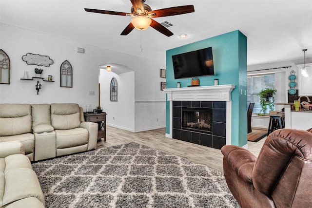 living room featuring a tiled fireplace, ceiling fan, and light wood-type flooring