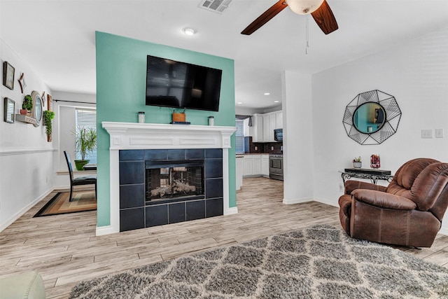 living room featuring ceiling fan and a tiled fireplace