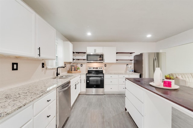 kitchen featuring white cabinets, appliances with stainless steel finishes, light stone counters, and sink