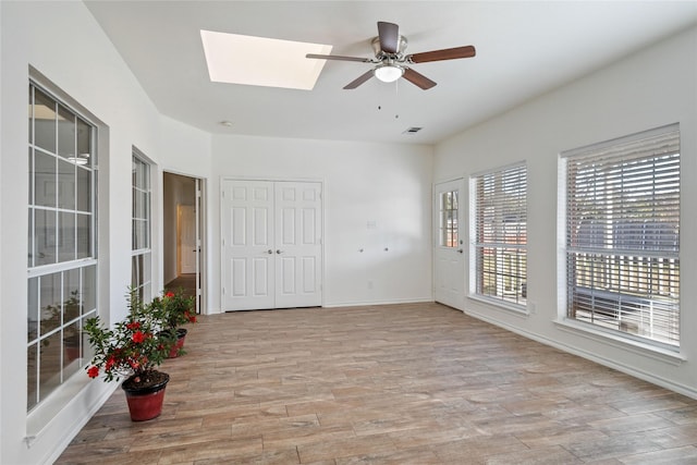 interior space with a skylight, ceiling fan, and light hardwood / wood-style floors