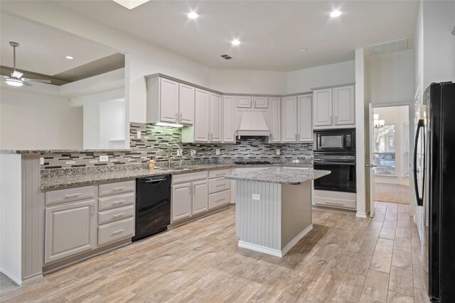 kitchen featuring light stone countertops, premium range hood, a kitchen island, and black appliances