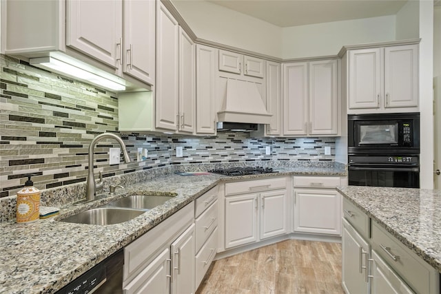 kitchen featuring white cabinetry, sink, premium range hood, backsplash, and black appliances