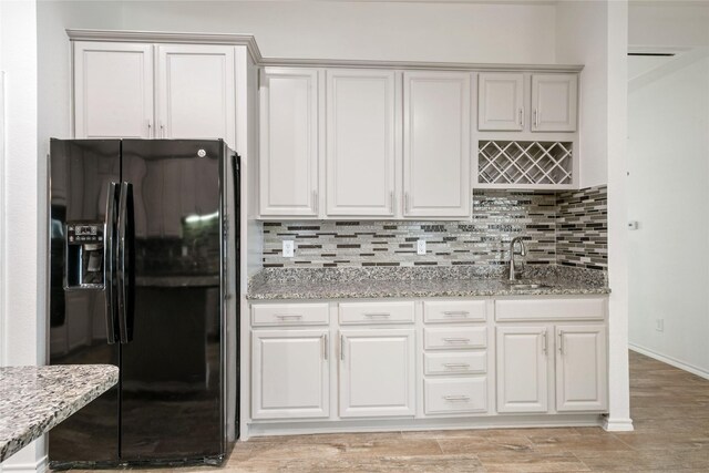 kitchen with light stone countertops, white cabinetry, and black fridge