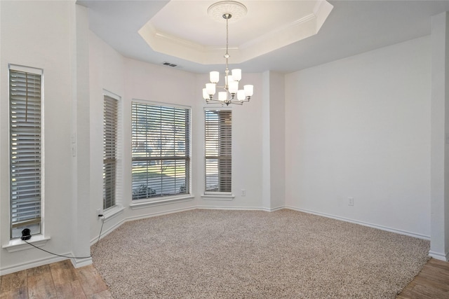 empty room featuring a tray ceiling, hardwood / wood-style floors, and an inviting chandelier