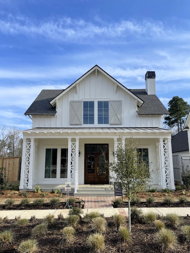 modern farmhouse style home featuring a standing seam roof, covered porch, a shingled roof, a chimney, and board and batten siding