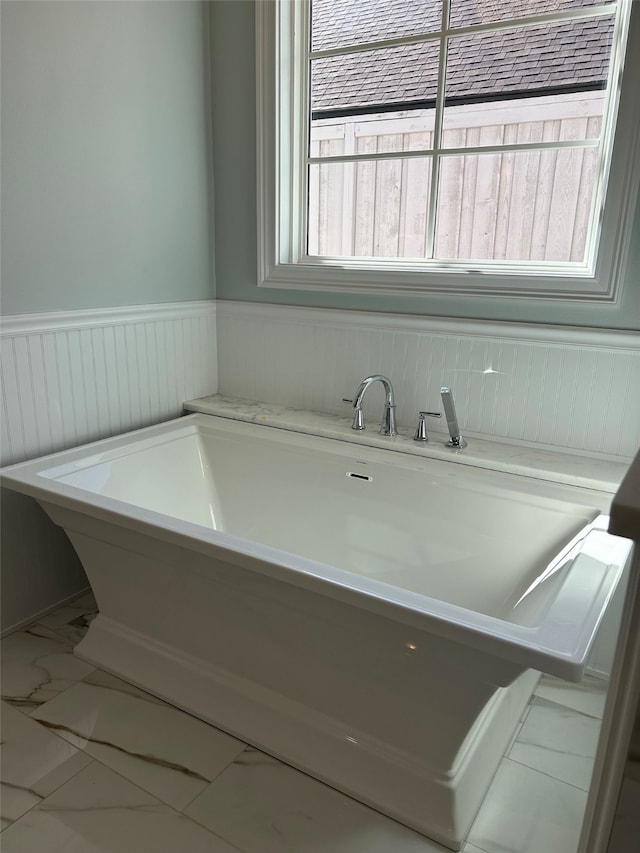 full bath with a freestanding tub, marble finish floor, and wainscoting