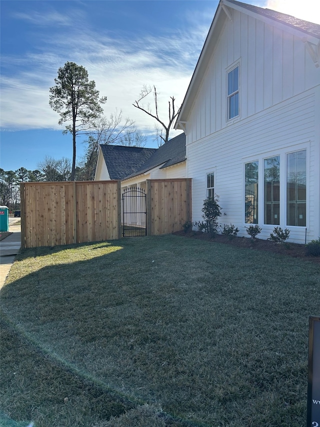 view of side of home with fence, a lawn, board and batten siding, and a gate