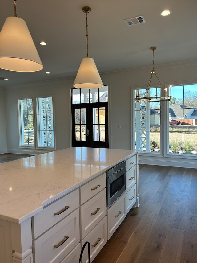 kitchen featuring light stone counters, stainless steel microwave, crown molding, and white cabinetry