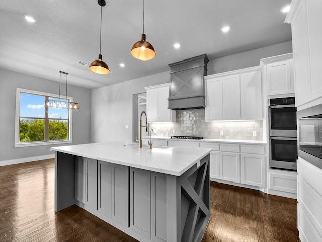 kitchen with double oven, a center island with sink, white cabinets, and hanging light fixtures