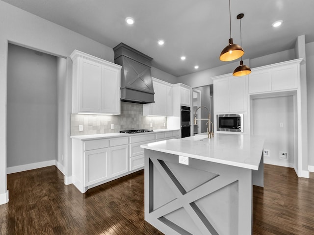 kitchen with decorative backsplash, built in microwave, decorative light fixtures, a center island with sink, and white cabinetry