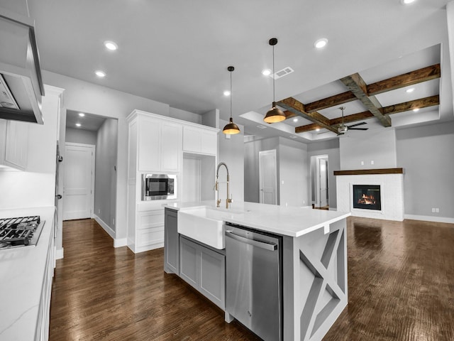 kitchen with an island with sink, decorative light fixtures, beam ceiling, white cabinetry, and stainless steel appliances