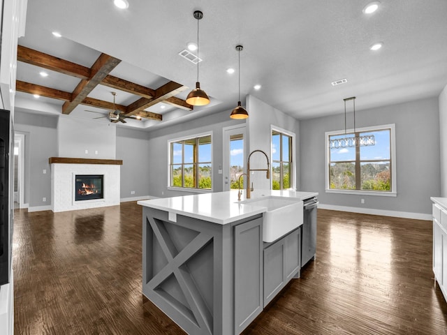 kitchen featuring pendant lighting, coffered ceiling, a center island with sink, sink, and beamed ceiling