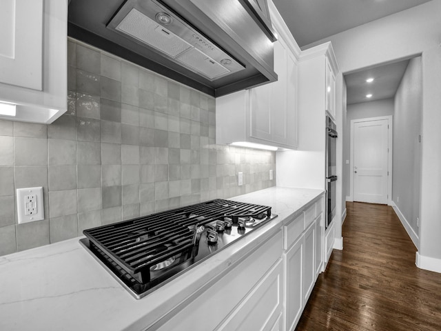 kitchen with light stone countertops, white cabinetry, stainless steel appliances, and wall chimney range hood